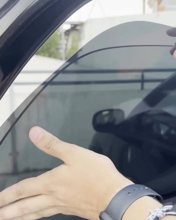 Mão a encostar a película ao vidro de uma porta traseira, sem água nem ferramentas